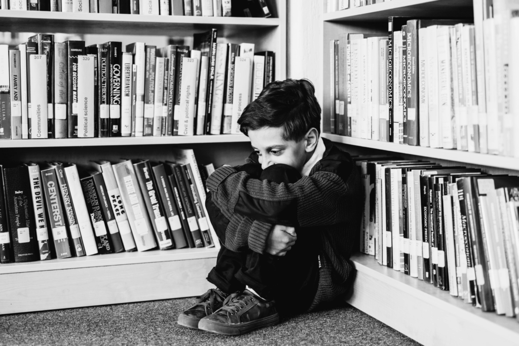 small child in corner of library bookshelves huddled because of trauma