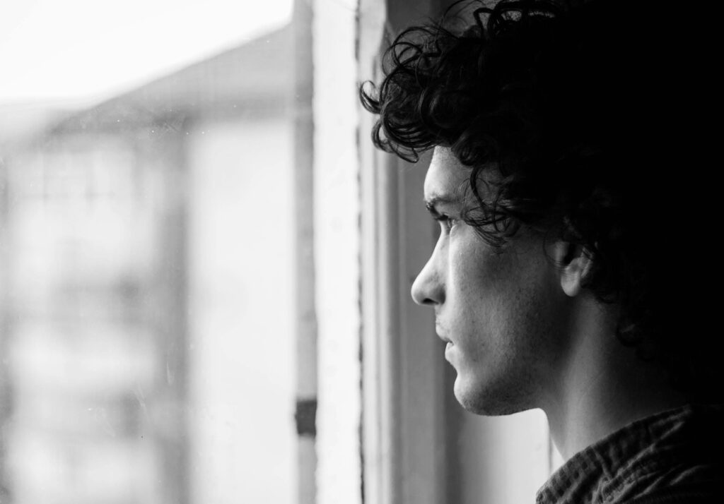 young man looking out window dealing with emotional trauma after injury